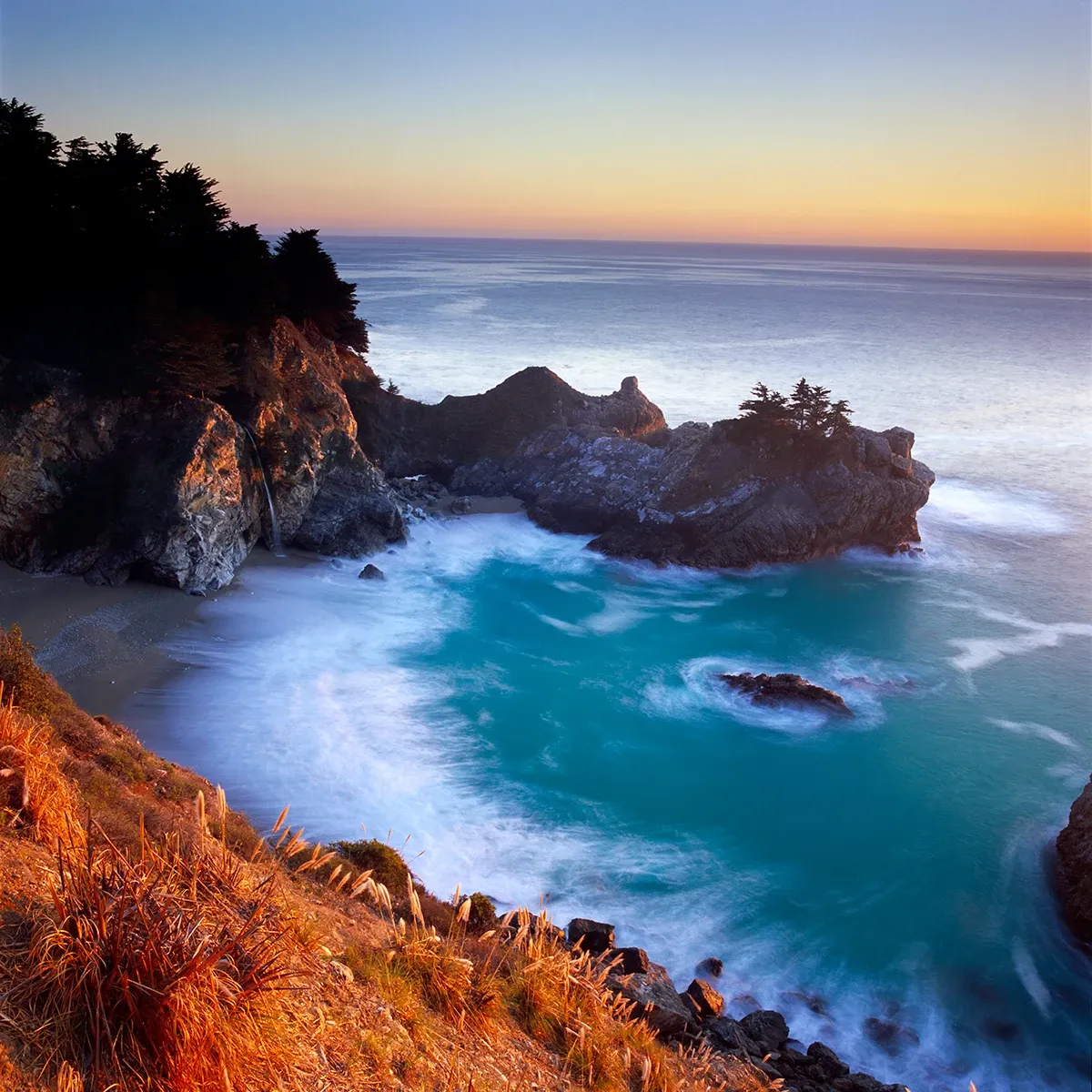 Sunset over a rocky cove with turquoise waves and orange cliffs