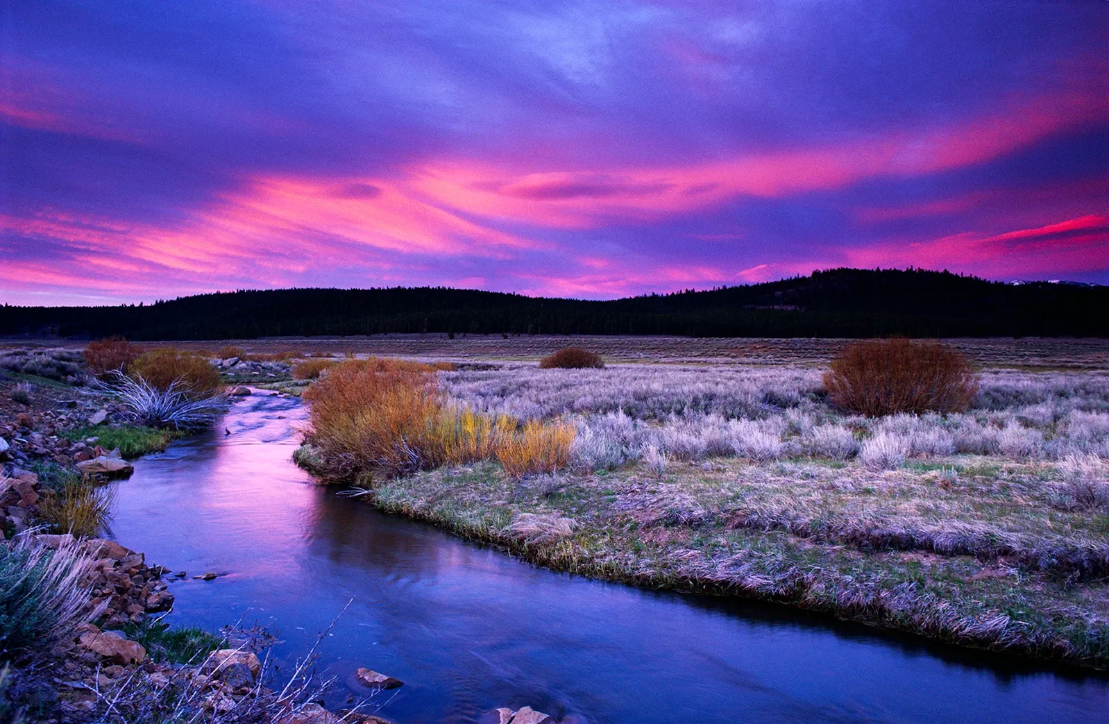Purple sunset over a winding river beside frosted grasslands and dark hills