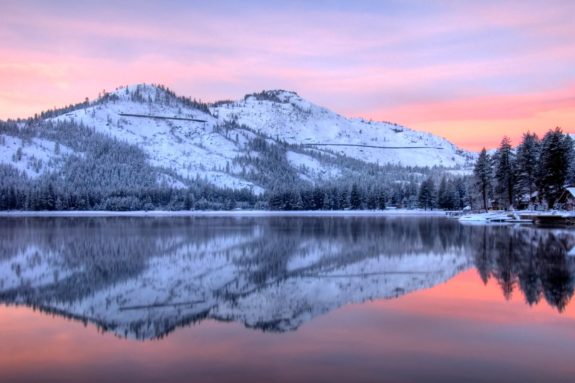 Snow-covered mountains reflected in a calm lake at pink sunset.