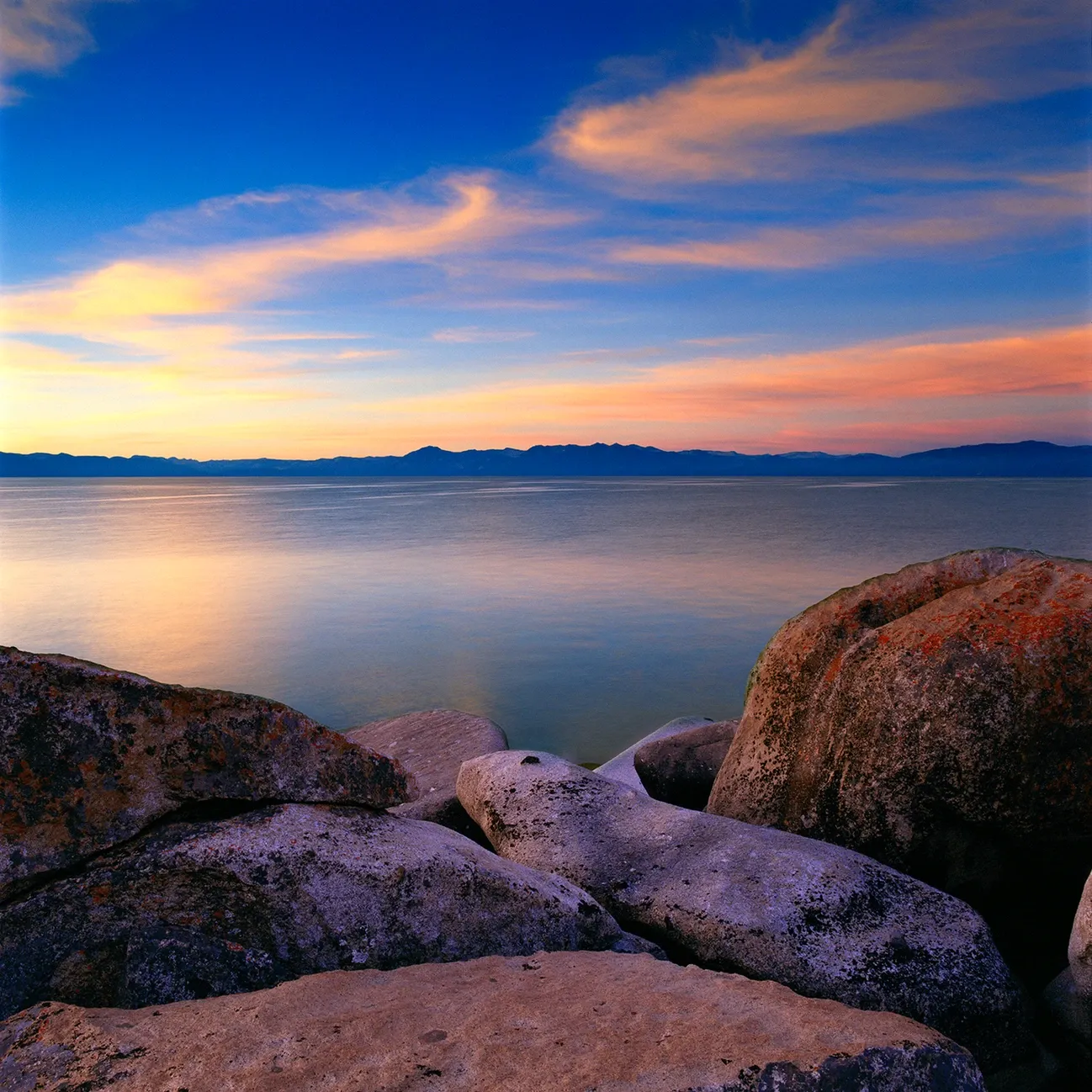 Rocky shoreline at sunset with calm water and a colorful blue-orange sky