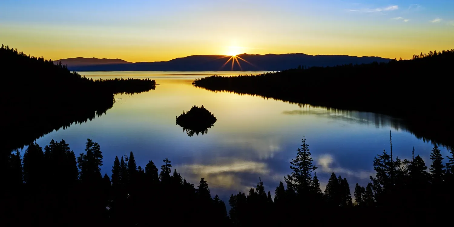Sunset over a calm lake reflecting a dark forest and island silhouette under a golden sky