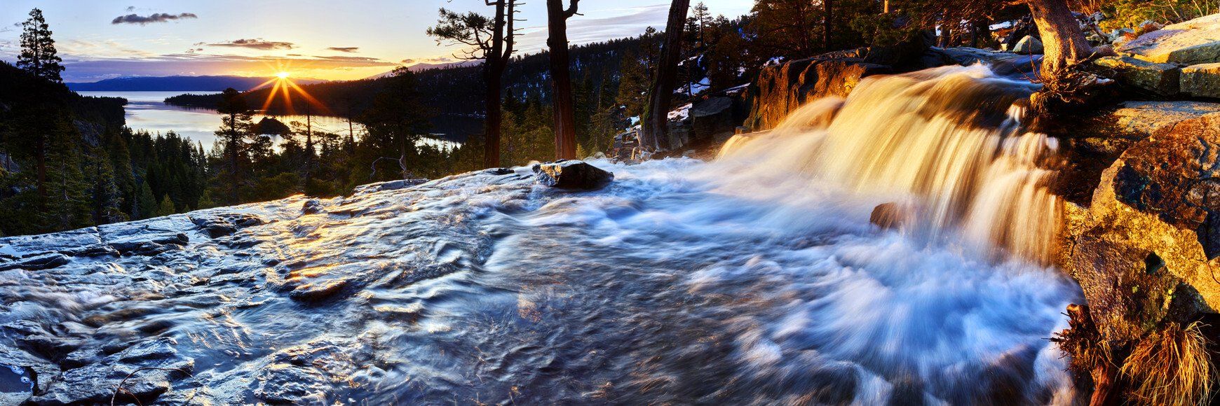 Sunset over a rushing waterfall and rocky river in a forested landscape