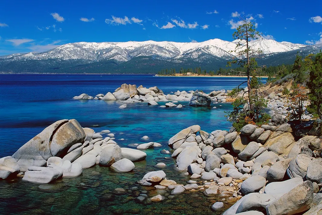 Rocky lakeshore with turquoise water, snow-capped mountains, and a clear blue sky