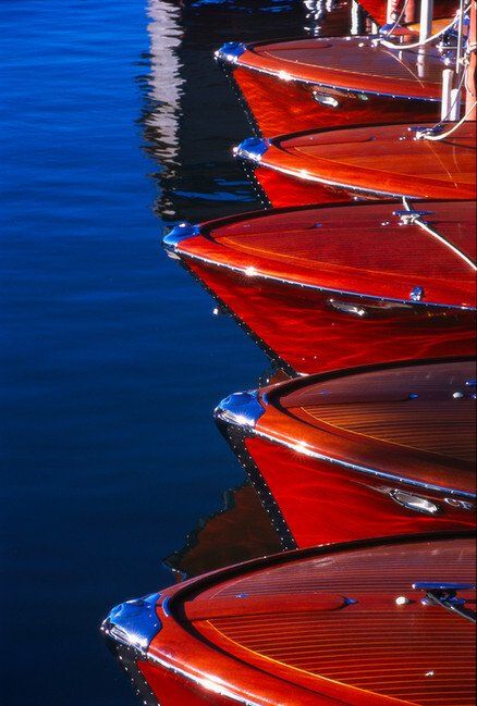Red canoes or kayaks stacked along blue water, with reflections shimmering nearby