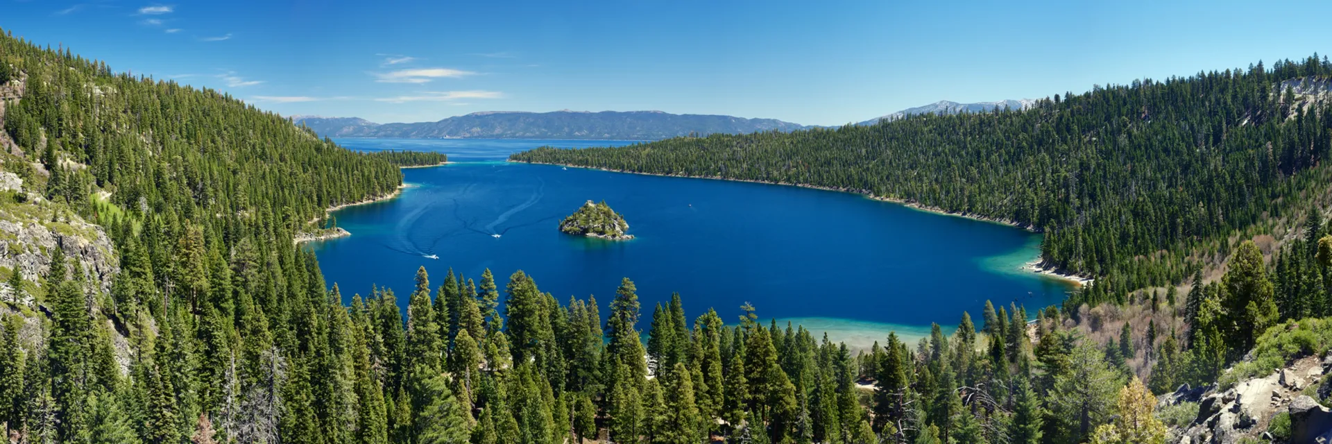 Blue mountain lake with a small island, surrounded by pine forests under a clear sky