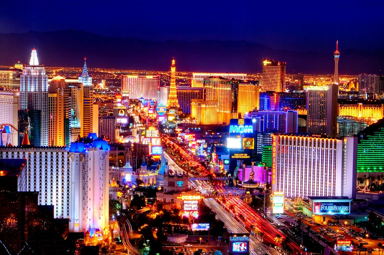 Bright neon city skyline at night with a busy illuminated boulevard and tall buildings
