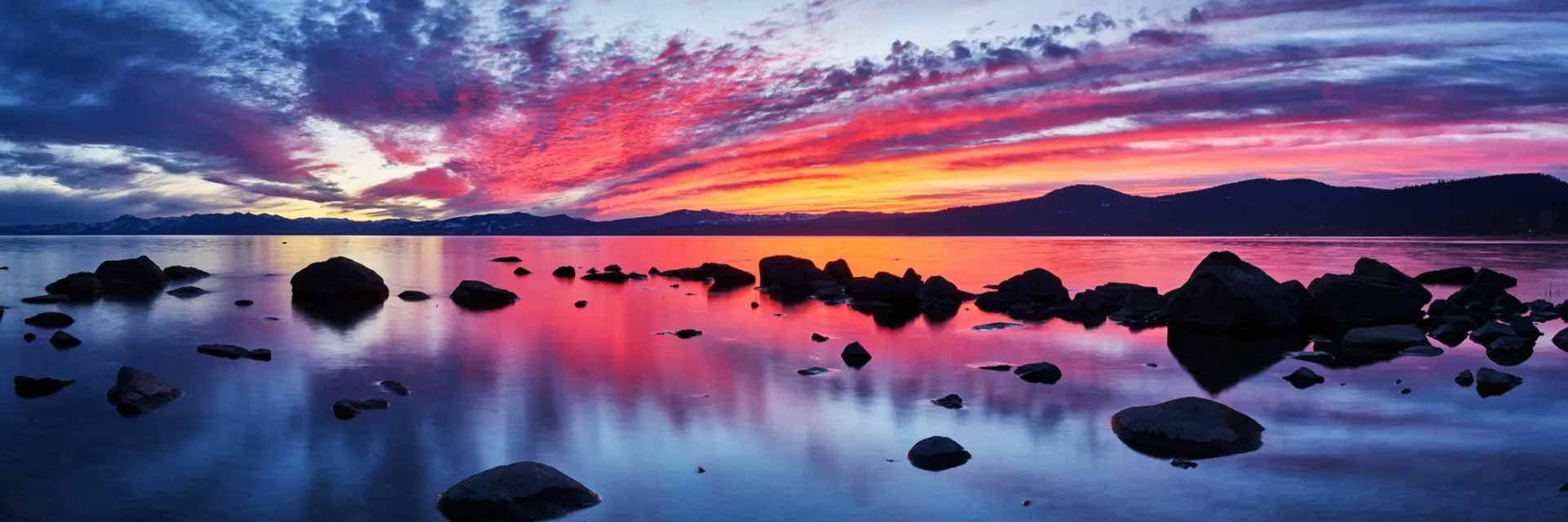 Purple and pink sunset reflected on calm water with dark rocks and silhouetted islets