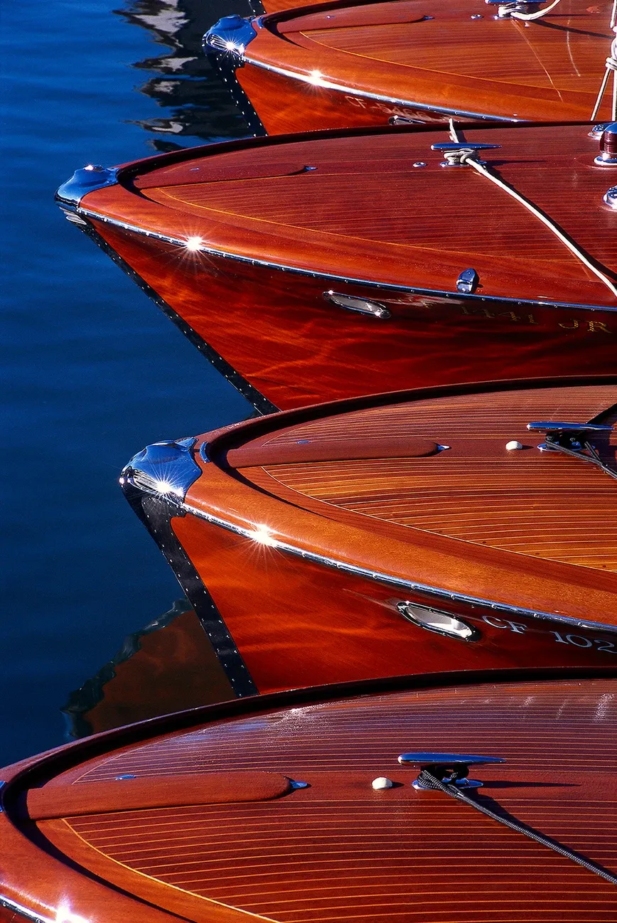 Close-up of glossy red wooden boat hulls lined up on blue water