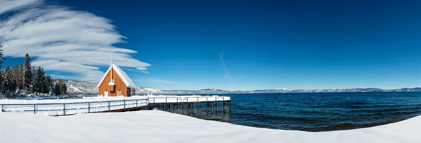 Snowy lakeside cabin with dock under a blue sky beside open water