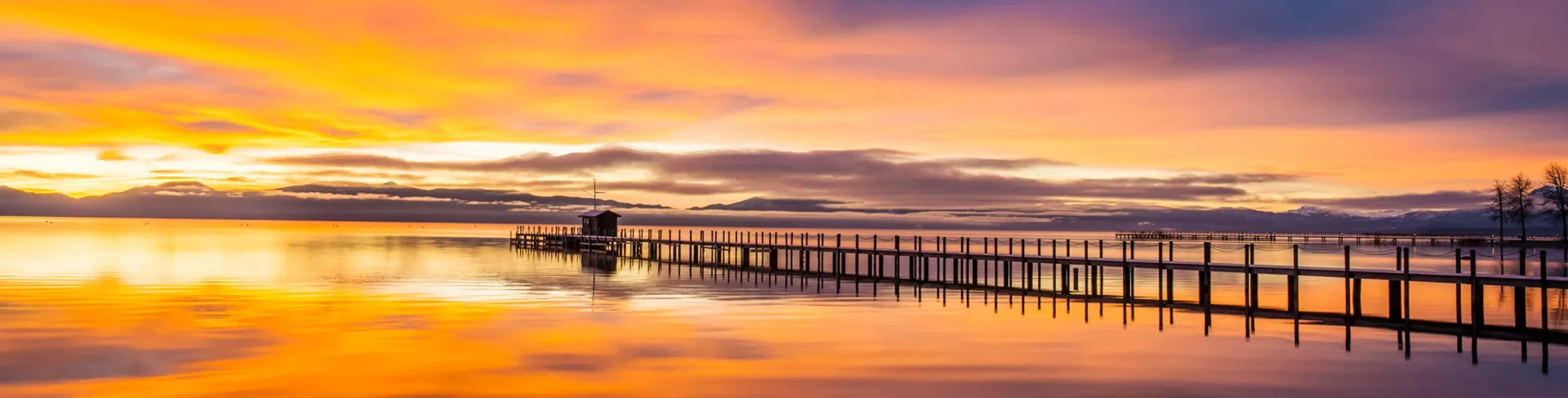 Sunset over a calm beach with a long pier silhouetted against orange and pink sky
