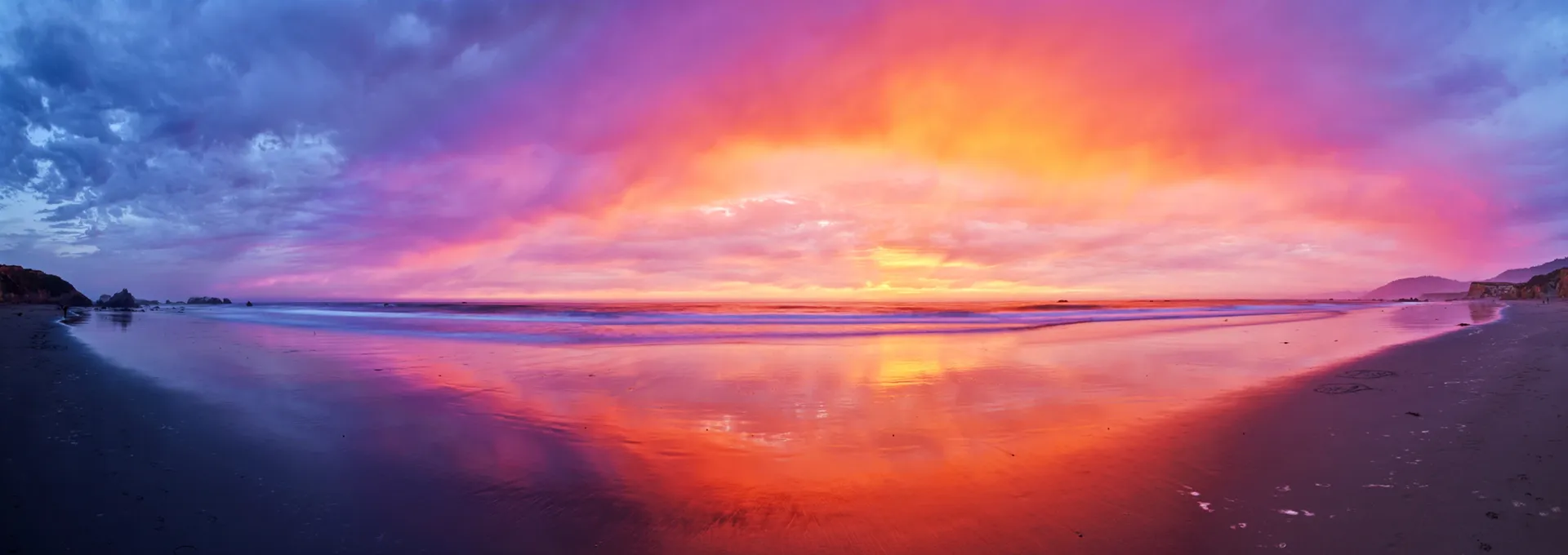 Vibrant sunset over calm water, with pink, purple, and orange reflections across the horizon