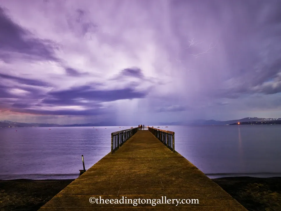 Wooden pier extending into a calm purple lake under dramatic cloudy dusk sky