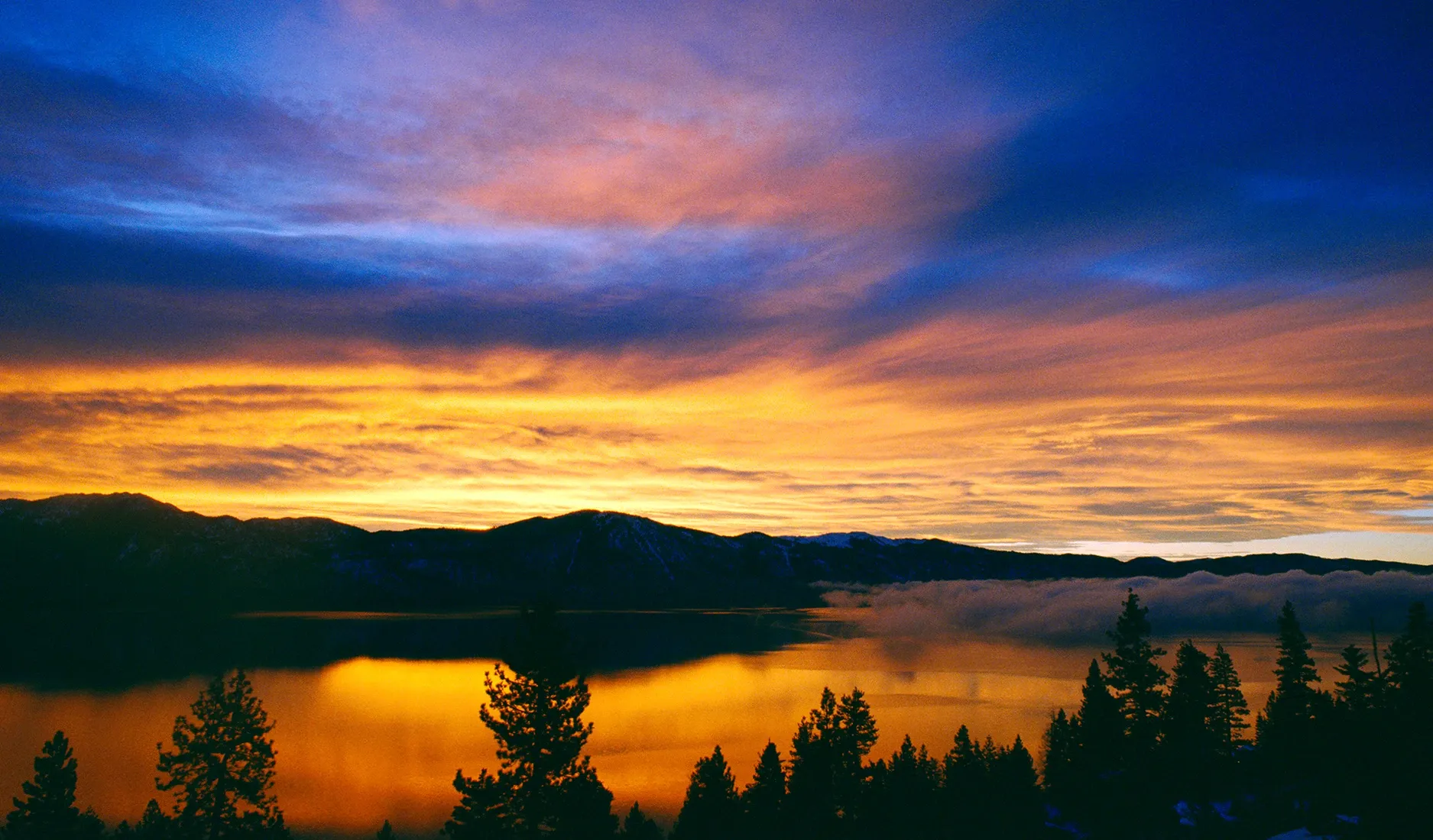 Sunset over a calm lake with silhouetted trees and colorful clouds in the sky