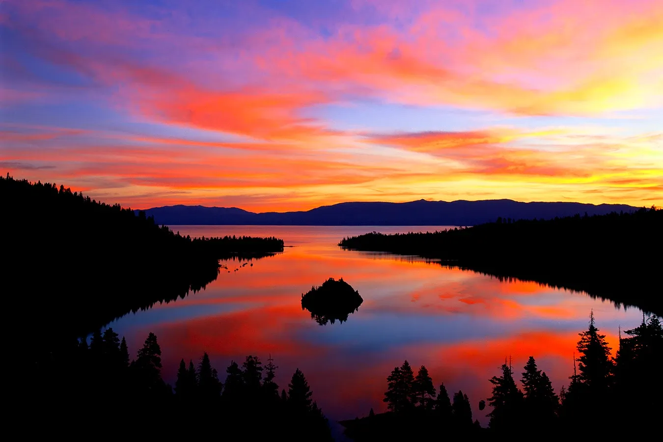 Vivid orange and purple sunset over a calm lake with silhouetted trees and islands