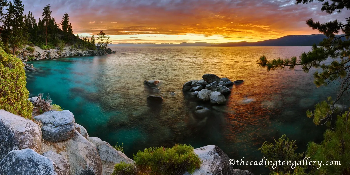 Turquoise lake at sunset with rocky shoreline, pine trees, and glowing orange sky