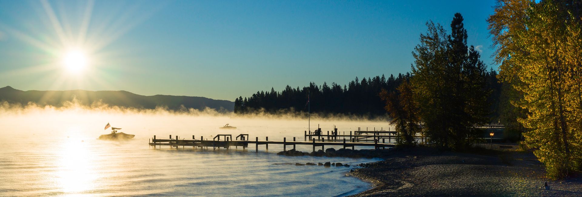 Sunrise over a foggy lake with a wooden dock and trees along the shoreline