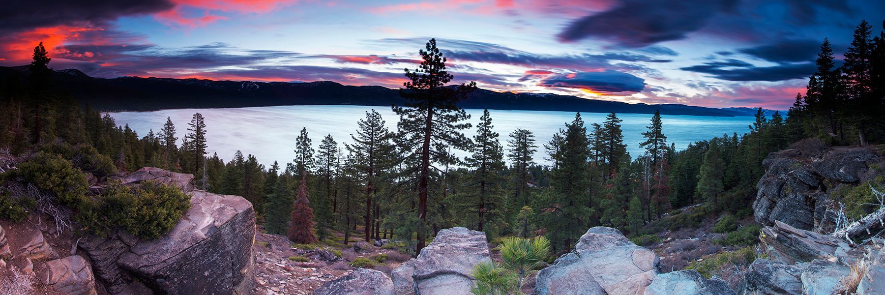 Sunset over a forested mountain overlook with pink, purple, and blue sky above rocky cliffs
