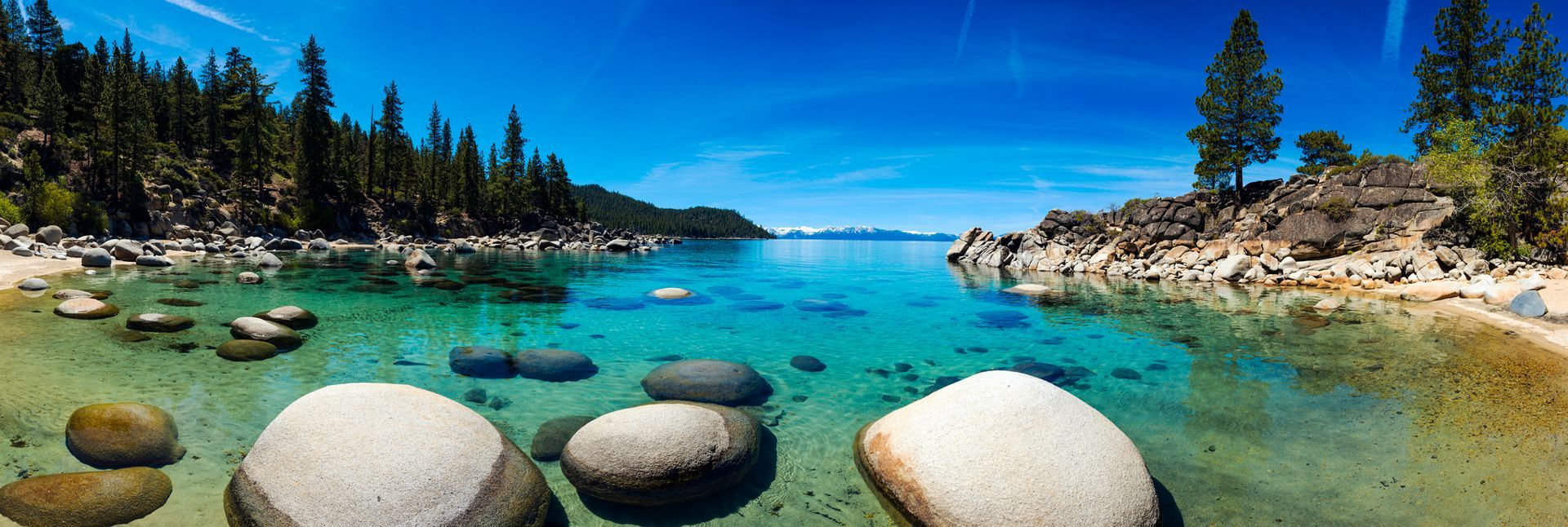 Rocky turquoise lake with clear water, pine trees, and a bright blue sky