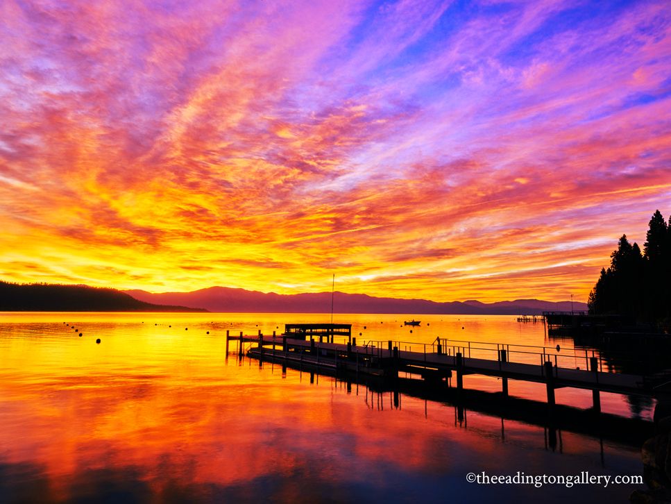 Vibrant orange-purple sunset over a calm lake with a silhouetted dock and distant trees