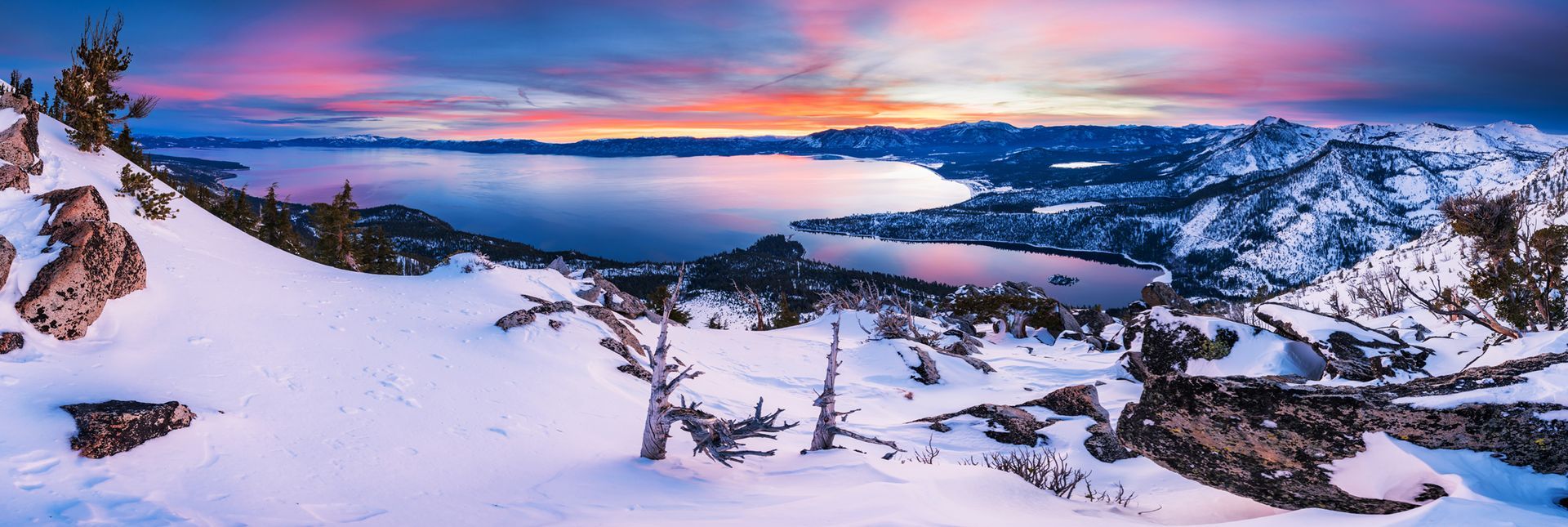 Snowy mountain landscape at sunset with a pink-blue sky and a frozen lake below.