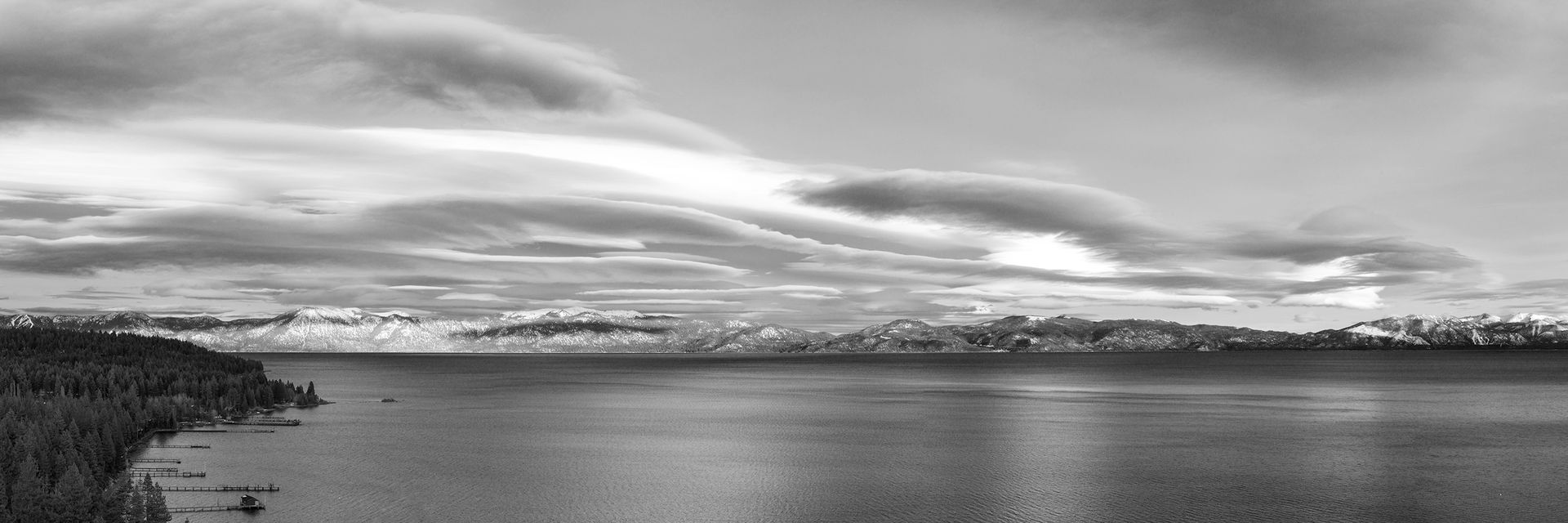 Black-and-white panoramic seascape with calm water, distant shoreline, and cloudy sky