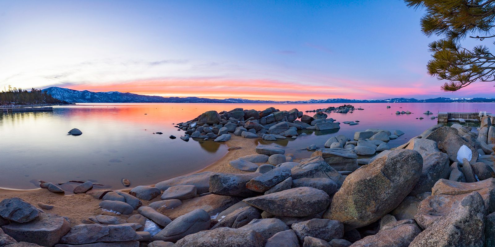 Rocky lakeshore at sunset with calm water reflecting a pink and blue sky