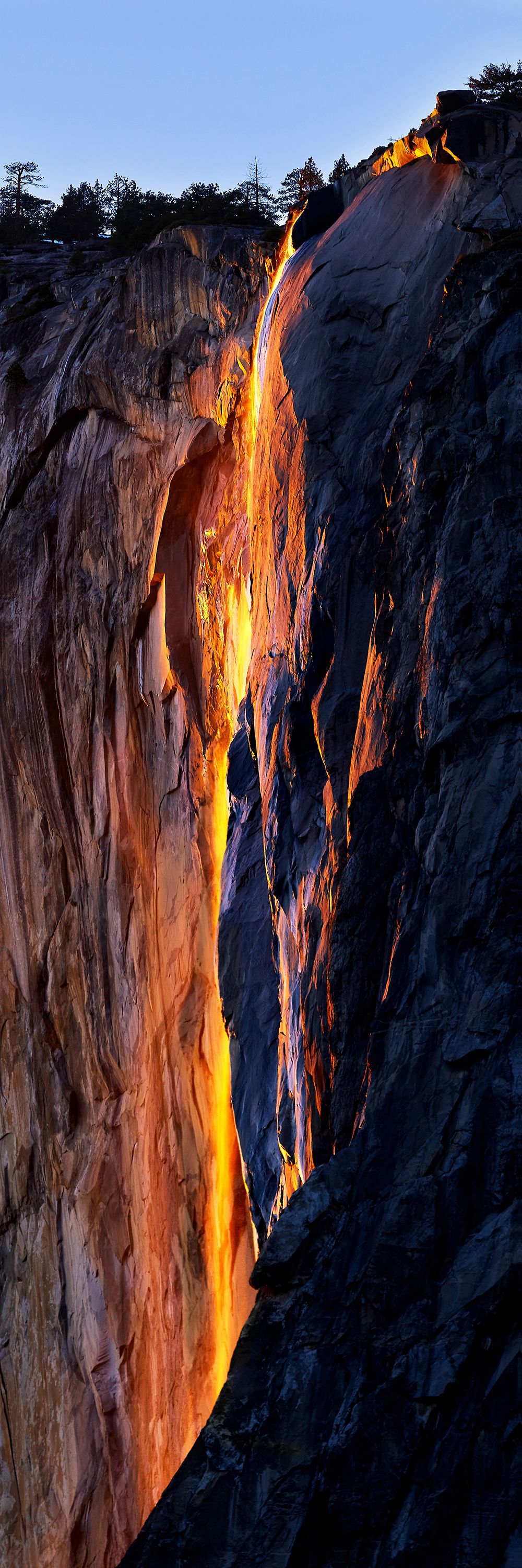 Glowing orange waterfall on a dark rocky cliff at dusk