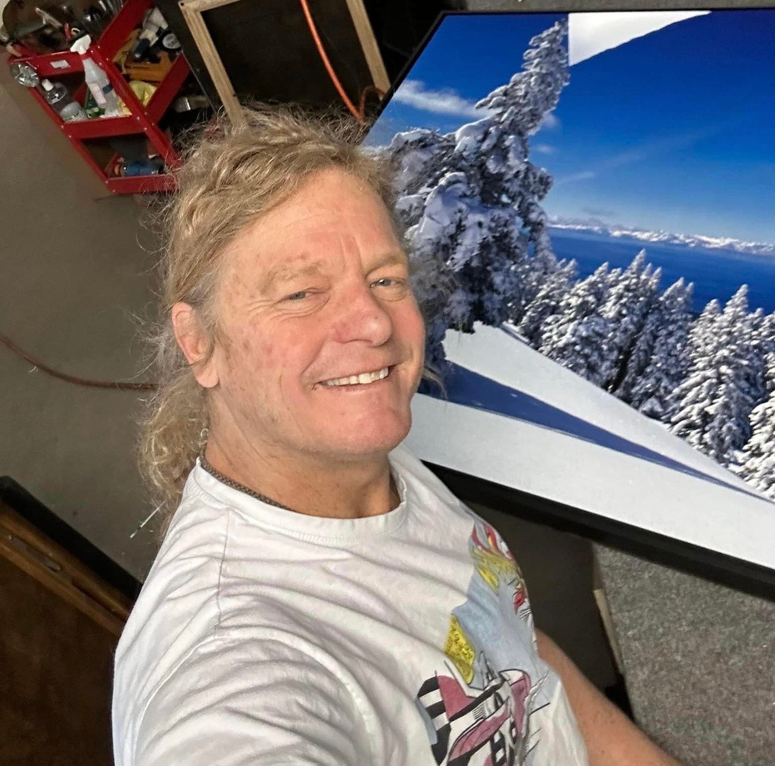 Smiling person taking a selfie beside a TV showing a snowy mountain scene