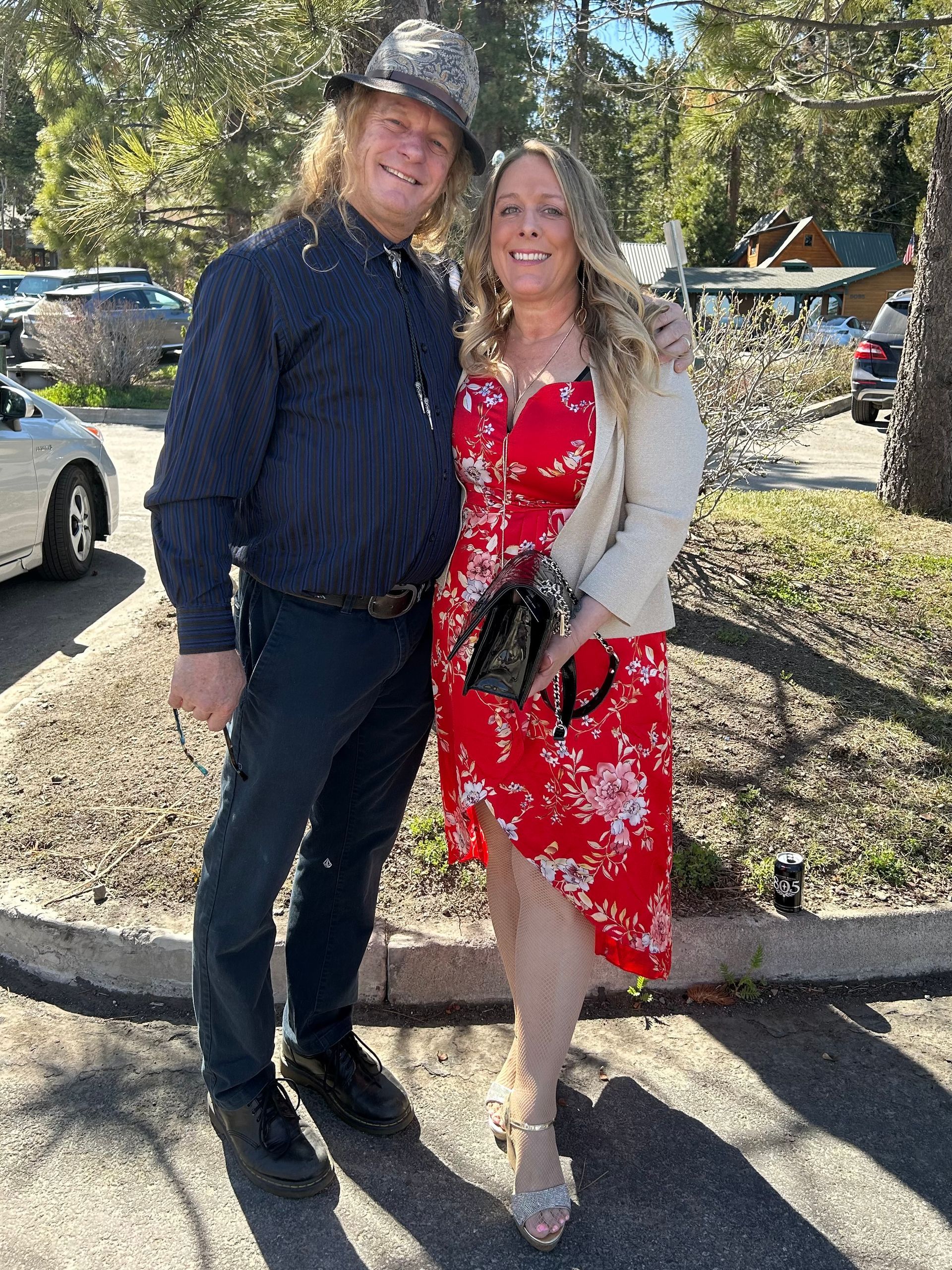 Two people smiling outdoors, standing together in sunlight on a sidewalk.
