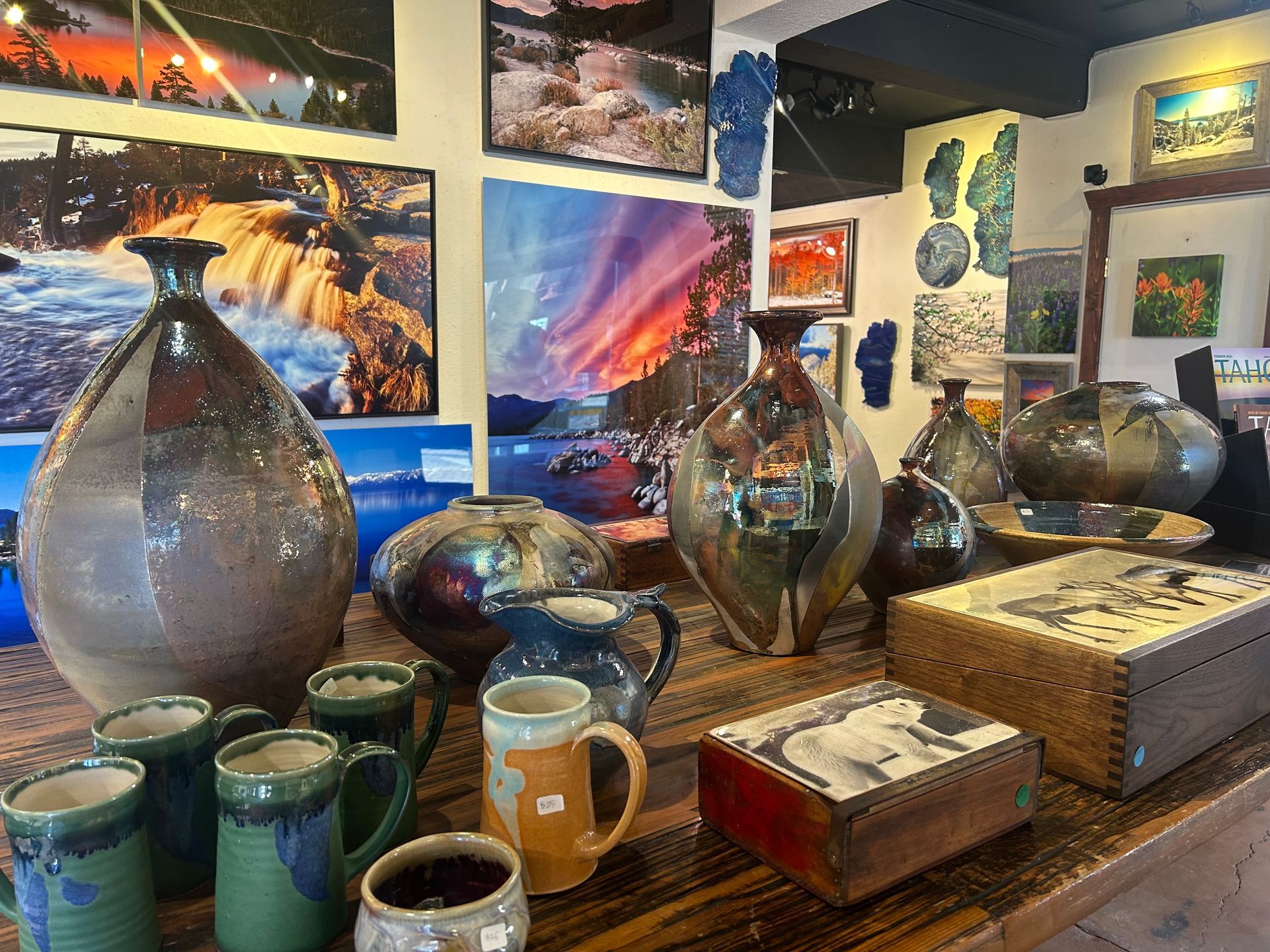 Ceramic vases, mugs, and boxes displayed on a wooden table in an art gallery.