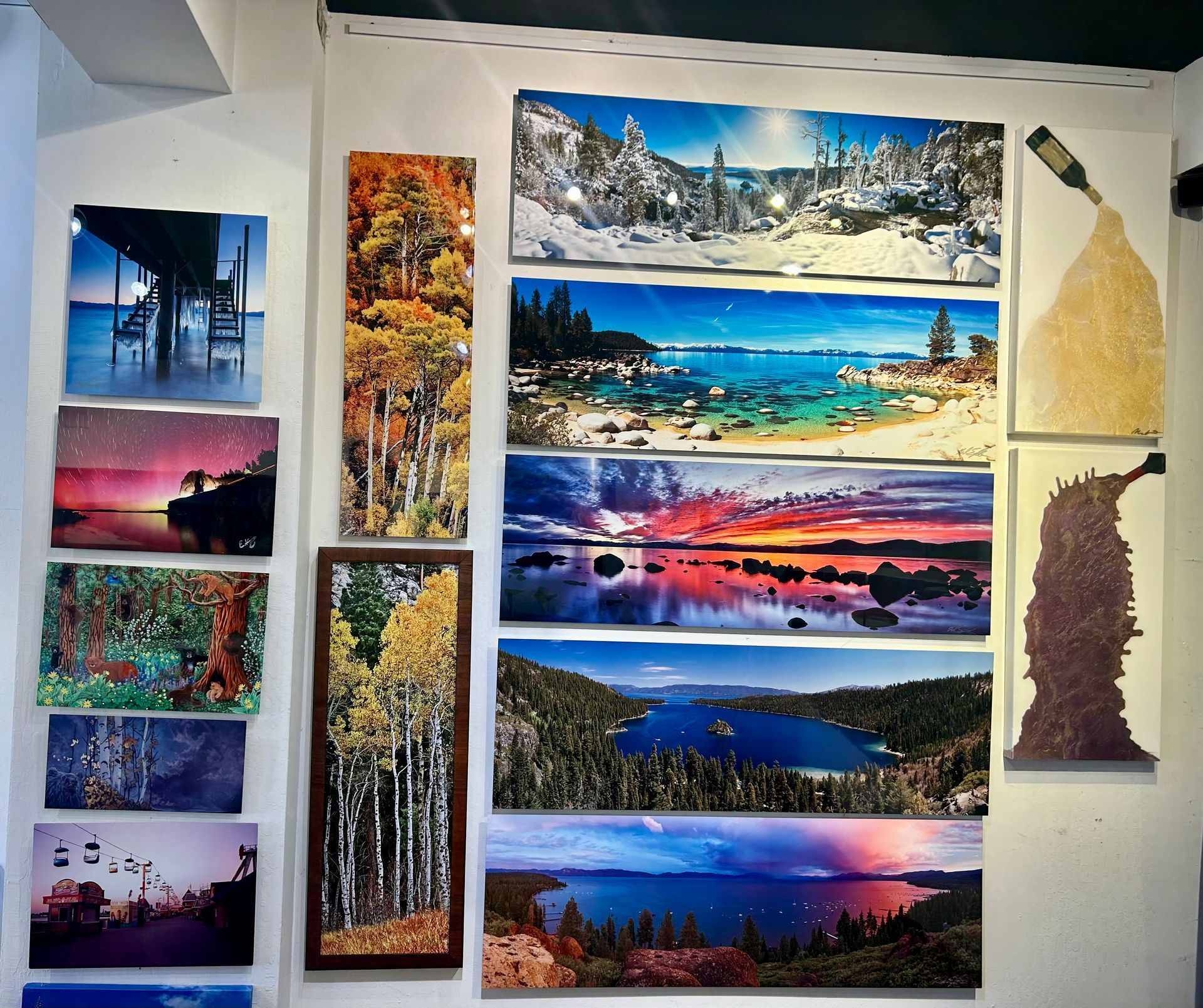 Wall of colorful landscape paintings and photos, including sunsets, mountains, forests, and coastal scenes.
