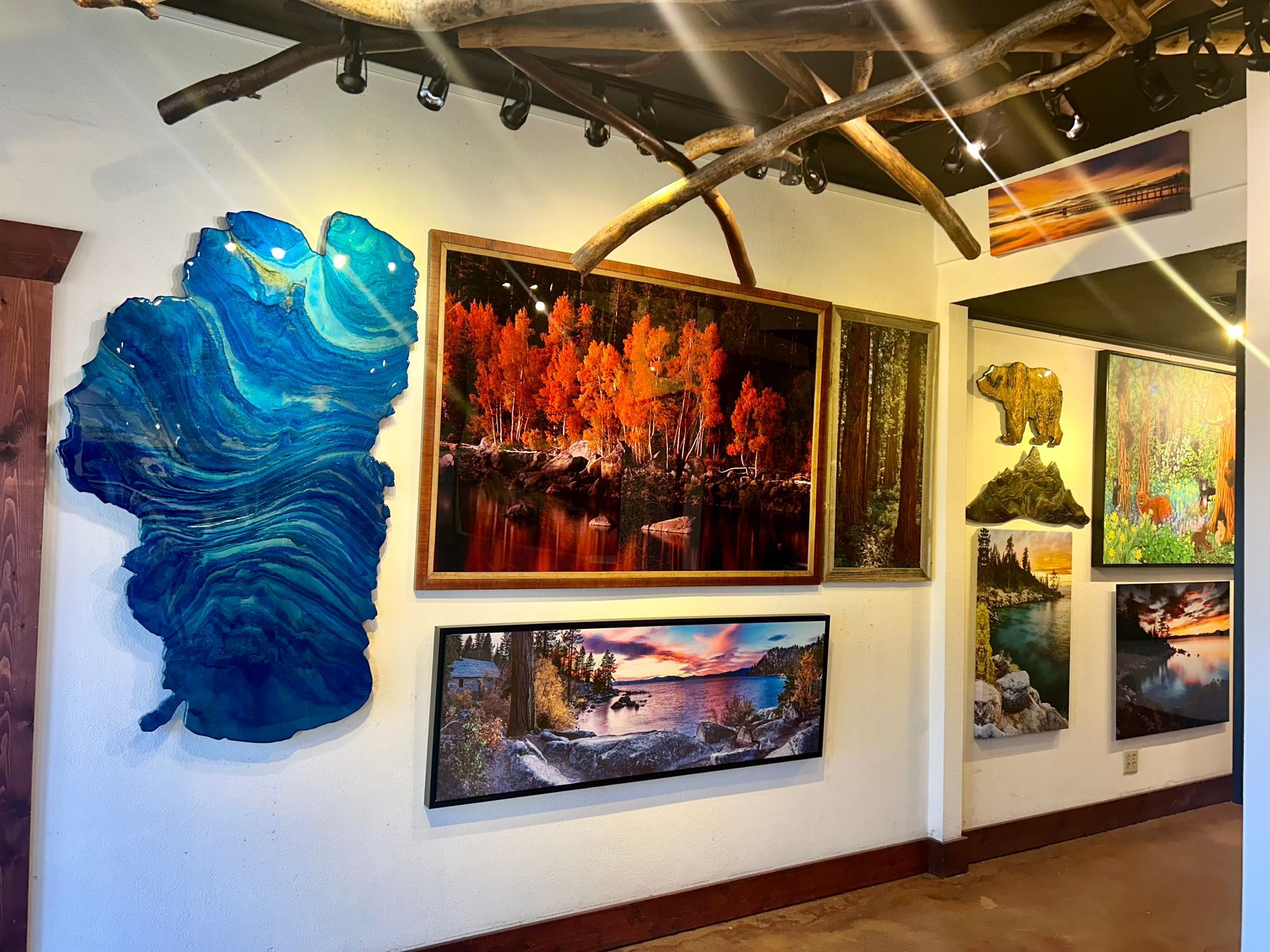 Art gallery wall with colorful abstract paintings, including a large blue textured piece and warm orange landscape scenes