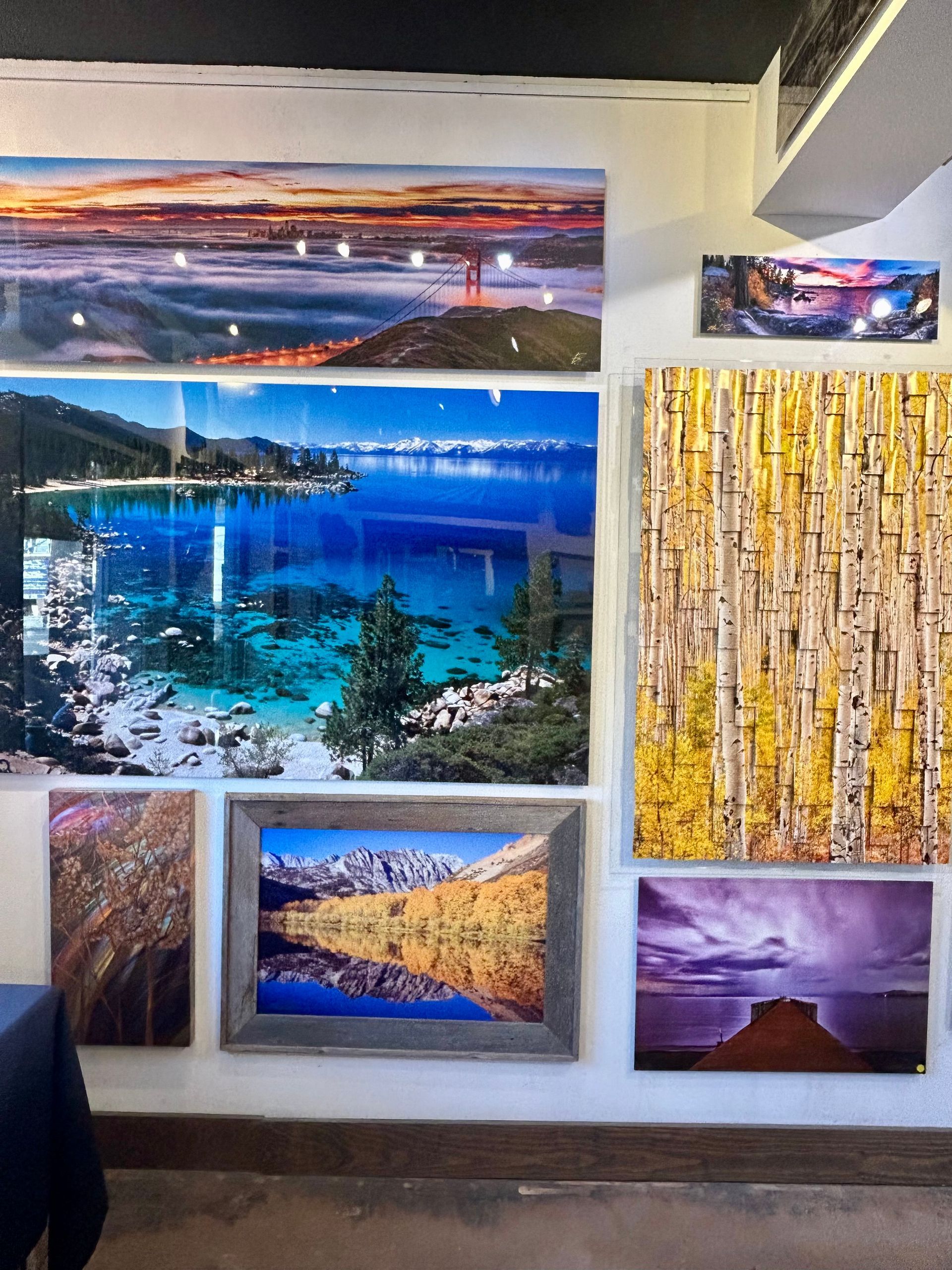 Wall display of colorful landscape photos, including lakes, mountains, and sunsets, in a gallery-like room