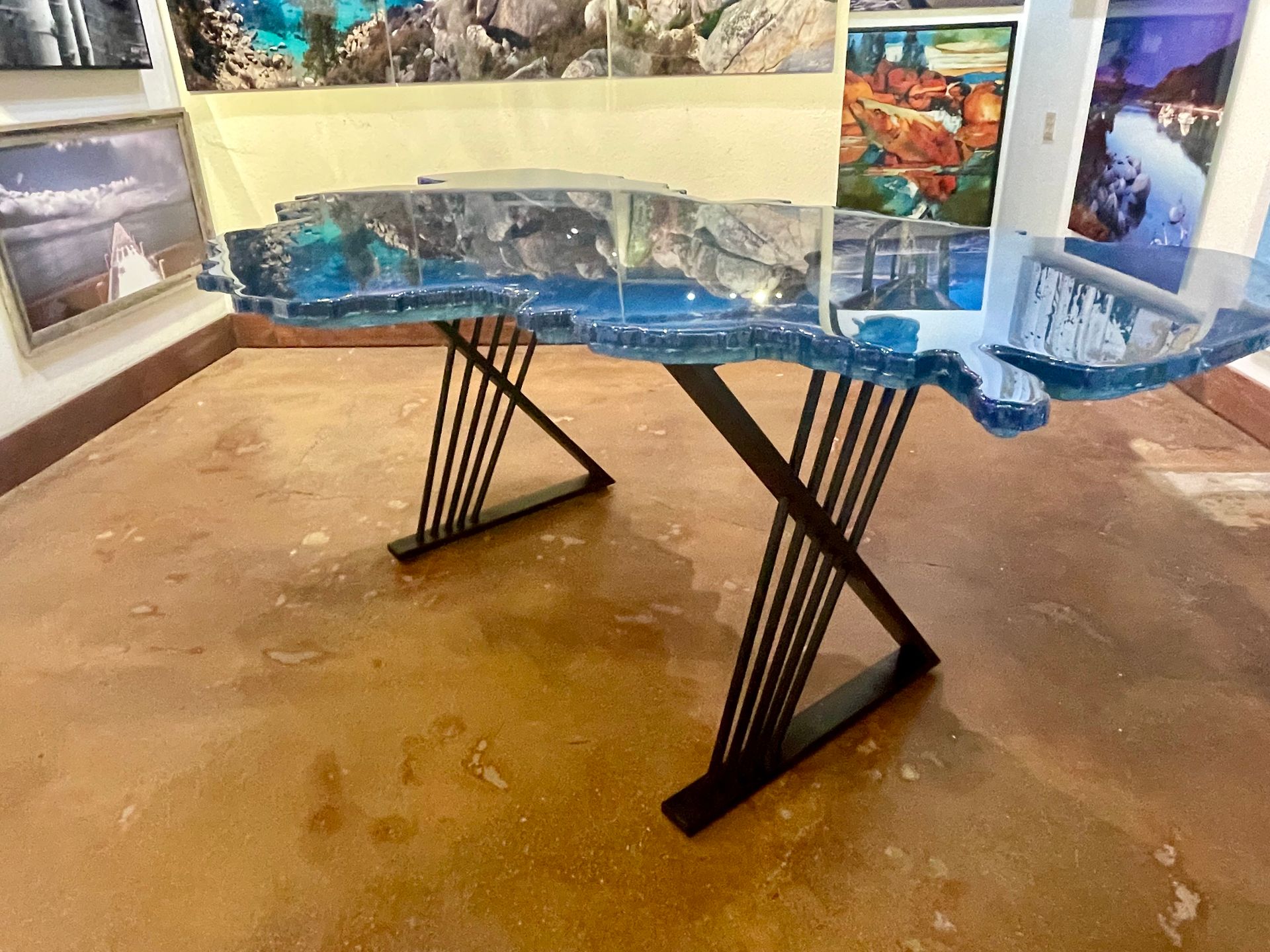 Abstract sculpture with blue glass top on black metal legs in a gallery room