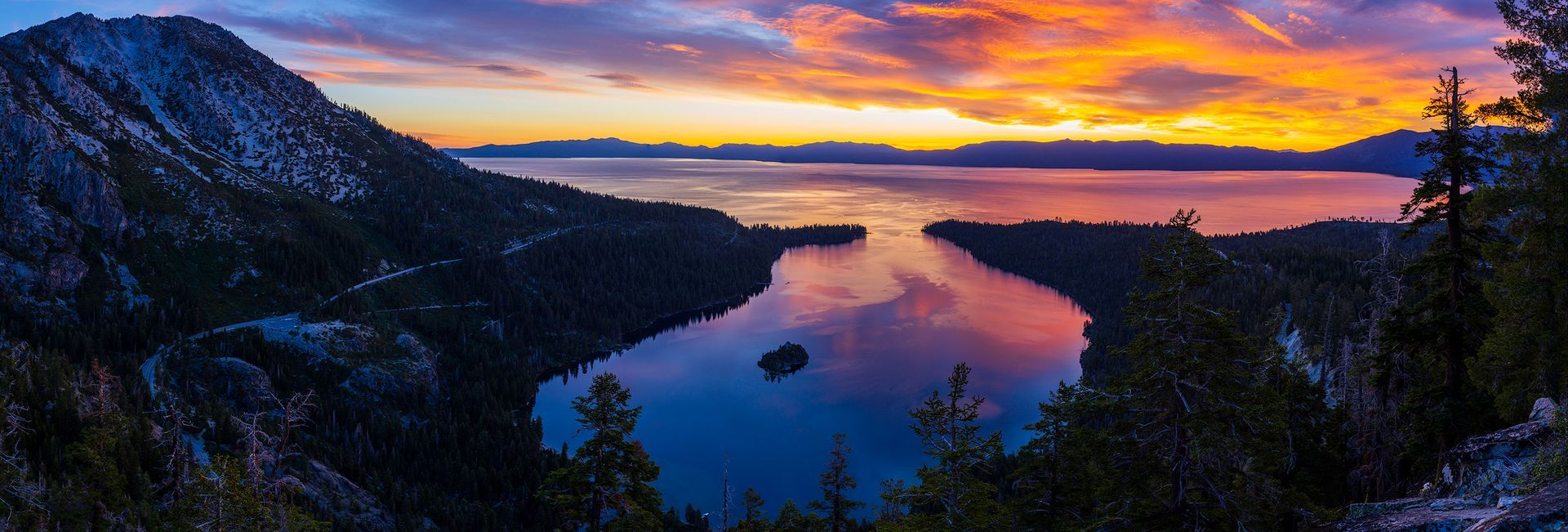 Sunset over a mountain lake with glowing clouds and dark forested hills reflected in calm water