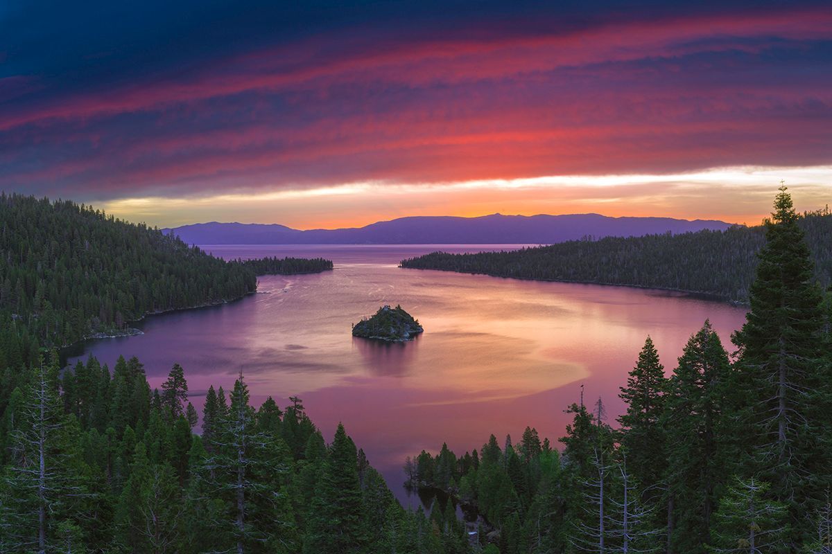 Sunset over a purple lake framed by pine forest and a small island