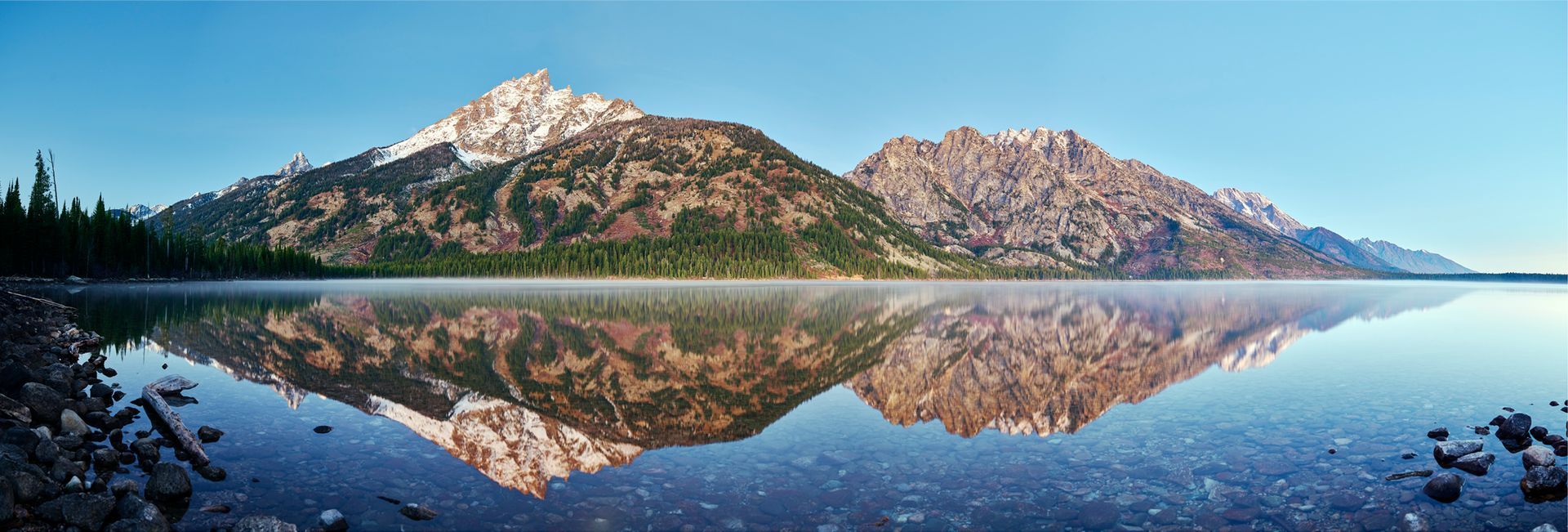 Snow-dusted mountains mirrored in a calm blue lake under a clear sky
