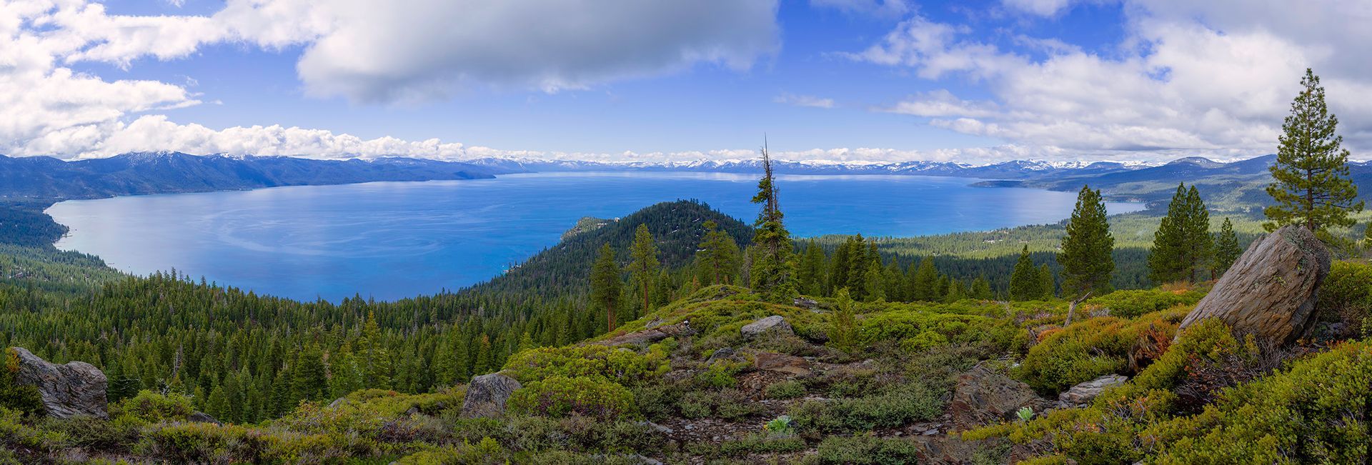 Panoramic mountain lake under a cloudy sky, with evergreen forest and rocky shoreline