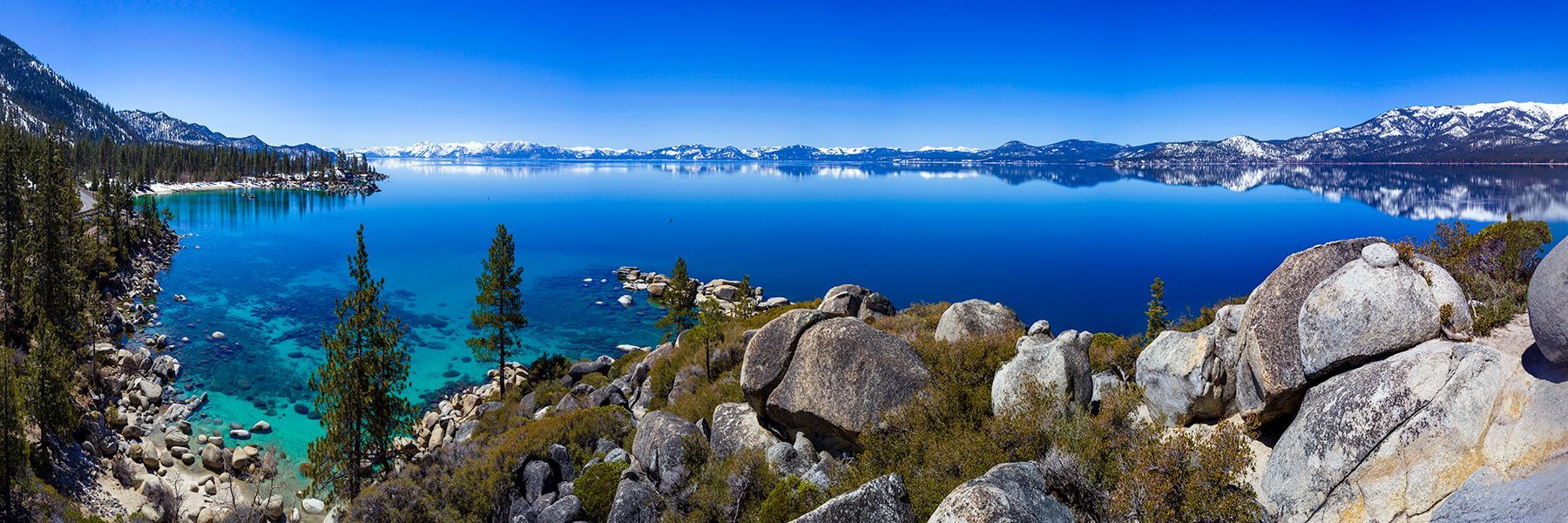 Snowy mountains and turquoise lake seen from a rocky forested overlook under a clear blue sky