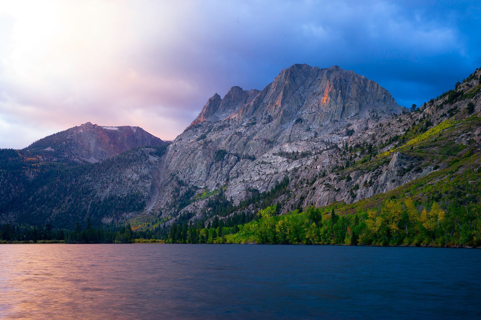 Mountain lake at dusk with rugged granite cliffs and pink-blue sky reflected on calm water