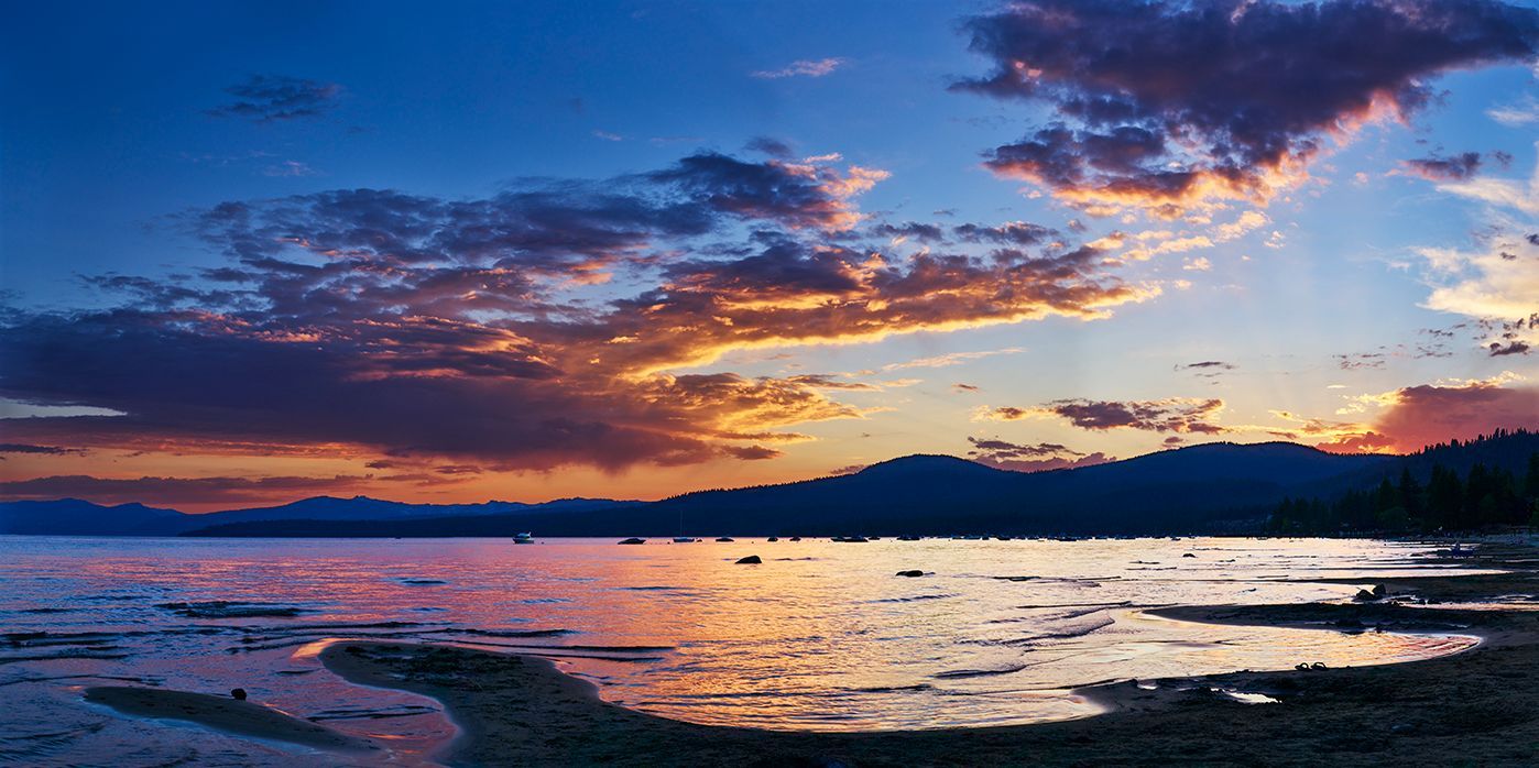 Sunset over a calm rocky shoreline with orange and blue clouds reflected on the water