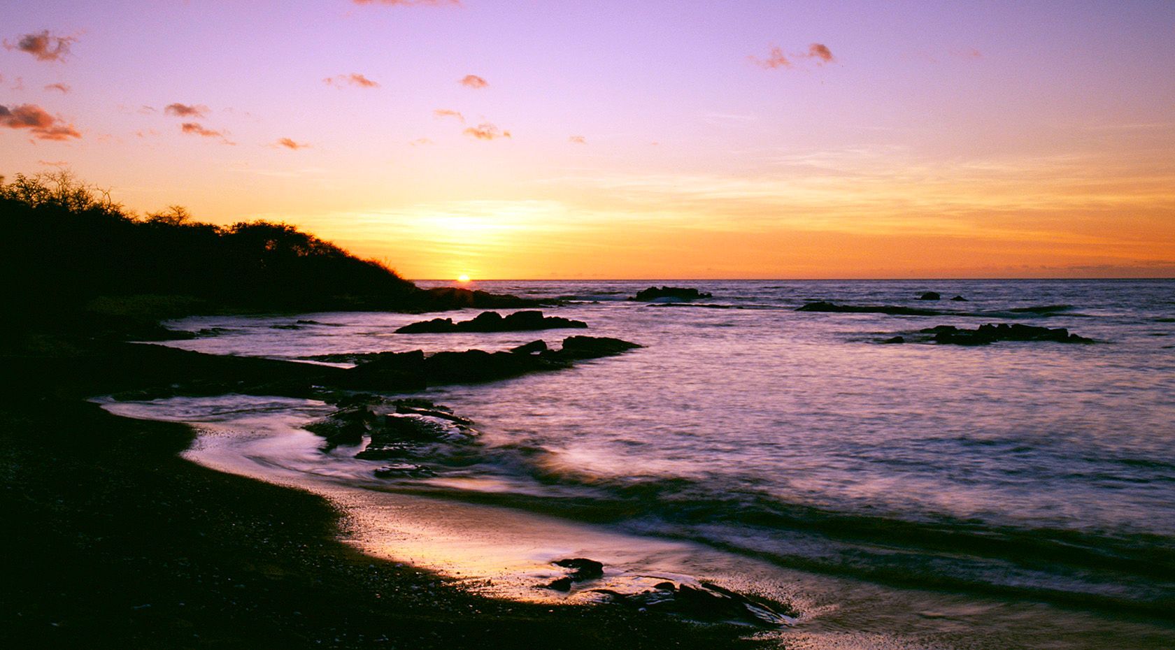 Sunset over a rocky shoreline with pink clouds and calm ocean waves