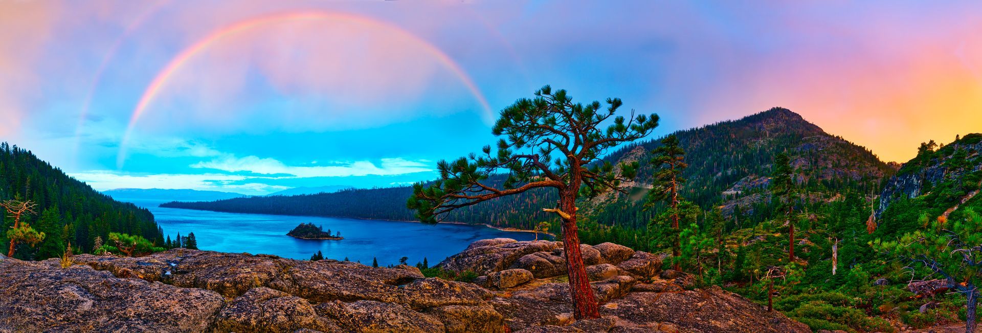 Colorful sunset over a lake with mountains, trees, and a rocky shoreline