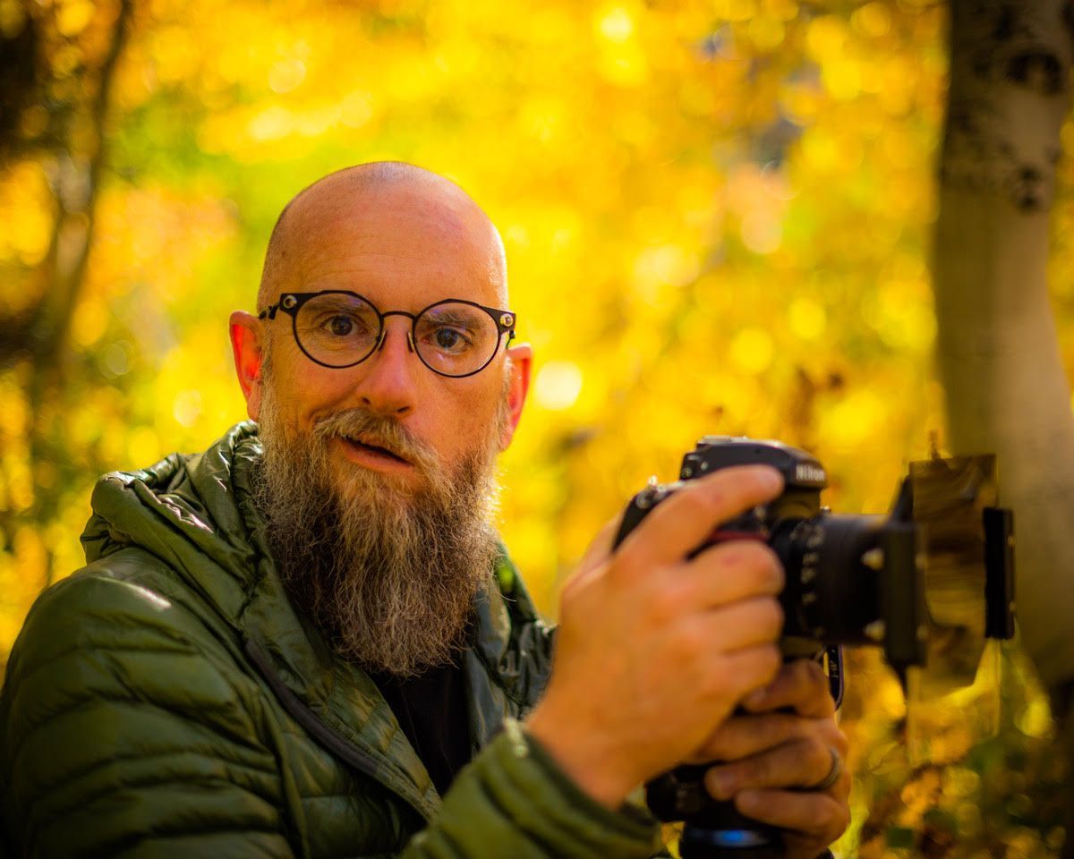 Man with glasses holding a camera in a golden autumn forest