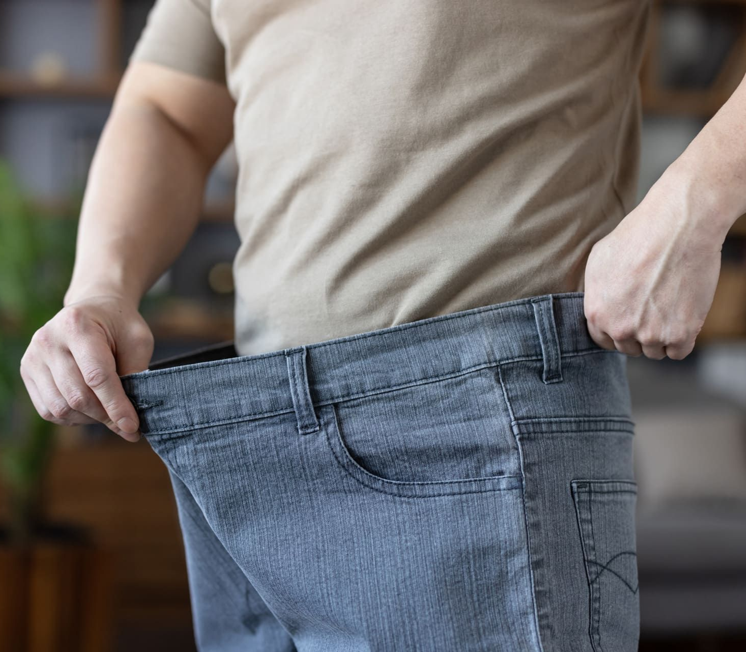 Man demonstrating successful weight loss and health transformation, holding out the waist of his loose, oversized jeans, symbolizing achievement in diet and fitness