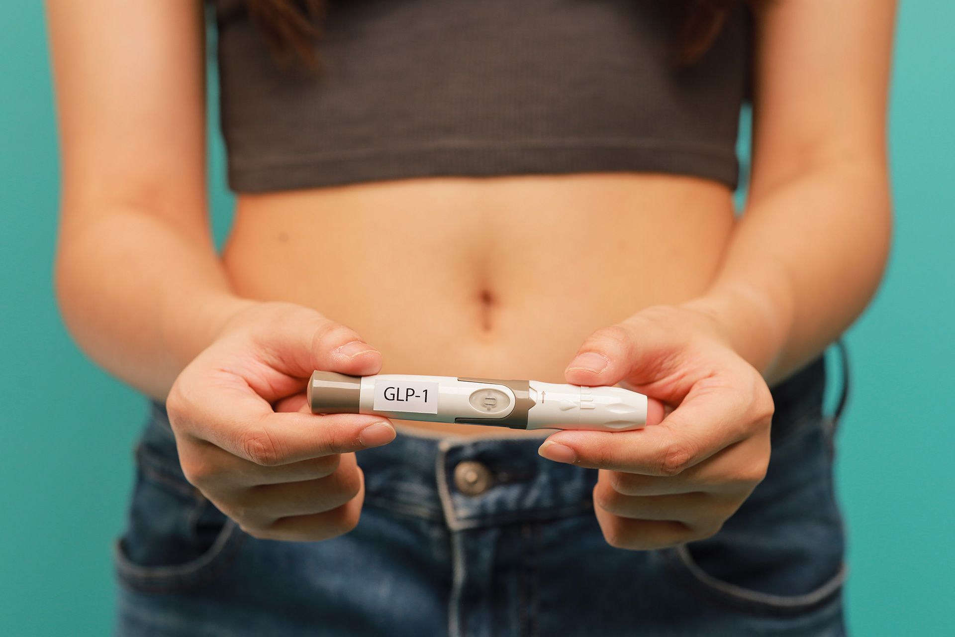 Weight loss transformation concept shown by woman holding GLP 1 injection pen in front of bare stomach for health and wellness