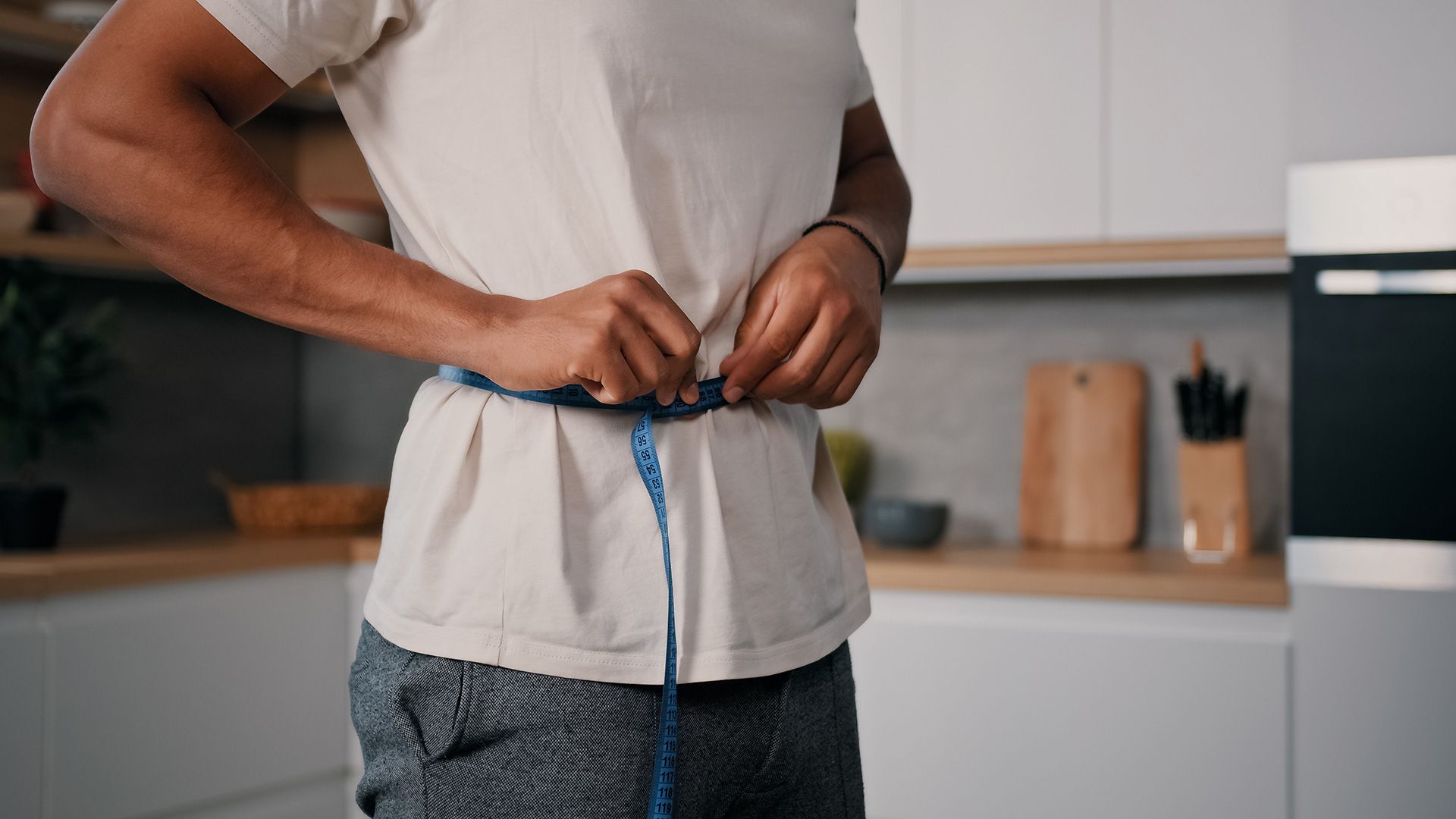 Unrecognizable sporty male sports man African guy measures waist with measuring tape check weight loss training workout sport dieting healthy nutrition control calories body muscle mass centimeters