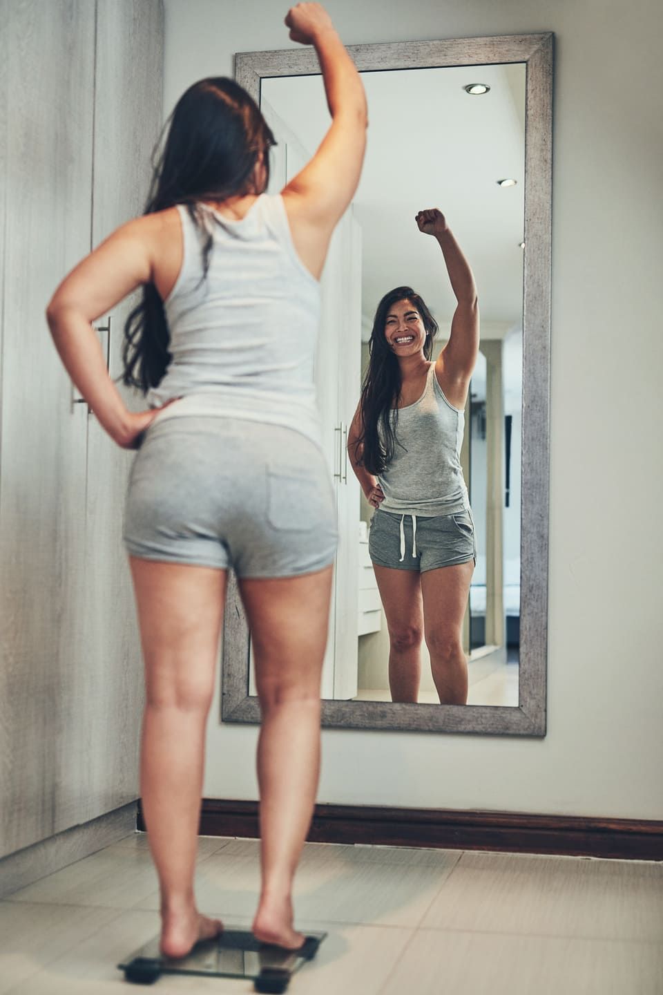 Celebration, weight loss goal and woman with scale and diet success in a home with mirror reflection. Cheering, happy and female person in a house with nutrition progress and a smile from wellness
