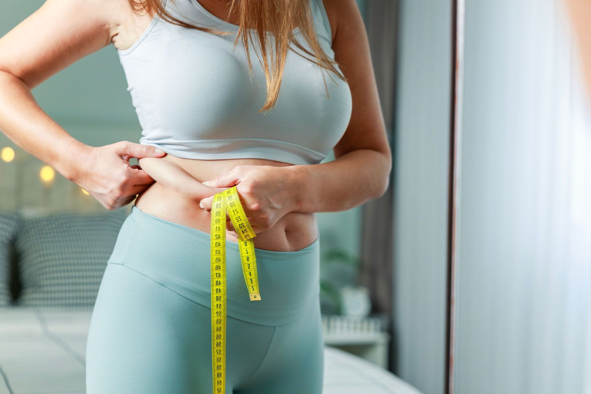 Fatty young woman hand holding excessive belly fat with measure tape, woman diet lifestyle