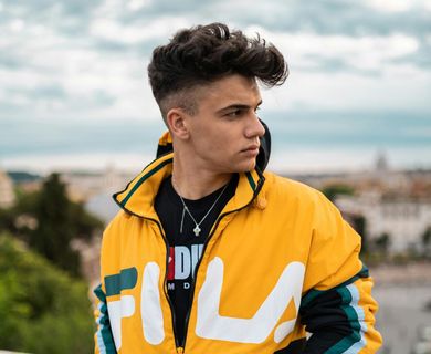 Young person in yellow jacket looks away from the camera, standing outdoors with a cityscape background.